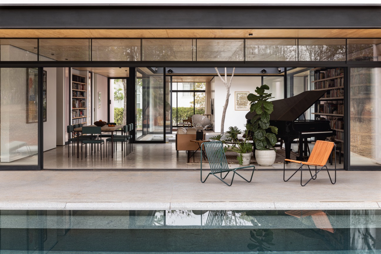 Vistas desde el patio del salón y comedor de una casa con amplios ventanales abiertos que cuenta con un piano negro.
